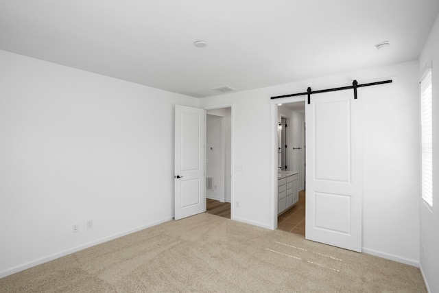 unfurnished bedroom featuring a barn door, connected bathroom, and light carpet