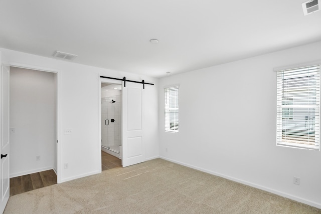 unfurnished bedroom featuring a barn door and light carpet