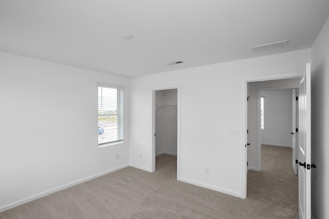 unfurnished bedroom featuring a walk in closet, light carpet, and a closet