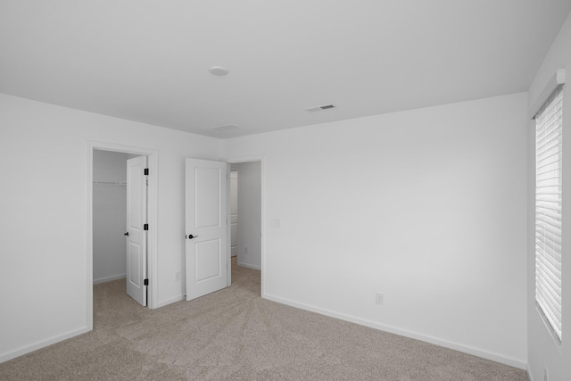 unfurnished bedroom with a spacious closet, light colored carpet, and a closet