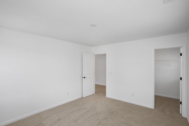 unfurnished bedroom with a walk in closet, light carpet, and a closet