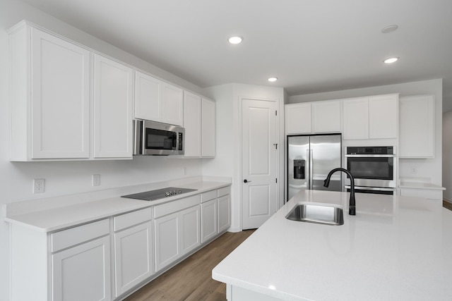 kitchen featuring appliances with stainless steel finishes, sink, white cabinets, hardwood / wood-style flooring, and a kitchen island with sink