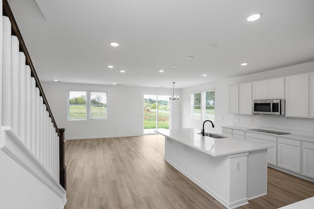 kitchen with sink, white cabinetry, decorative light fixtures, black electric cooktop, and a kitchen island with sink