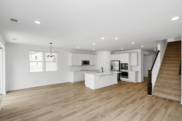 kitchen with light hardwood / wood-style flooring, stainless steel appliances, an island with sink, white cabinets, and decorative light fixtures