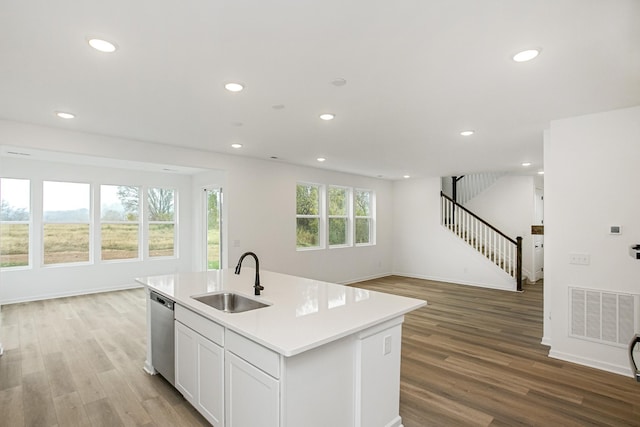 kitchen with stainless steel dishwasher, sink, white cabinetry, light hardwood / wood-style flooring, and an island with sink