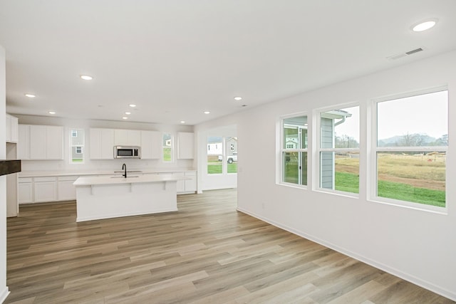 kitchen featuring light wood-type flooring, a kitchen island with sink, sink, and white cabinetry