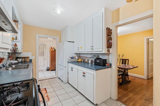 kitchen featuring sink, white cabinetry, light tile patterned floors, white fridge, and gas range oven