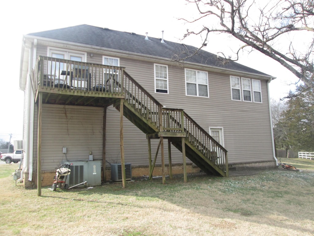 rear view of house with central AC unit, a deck, and a yard