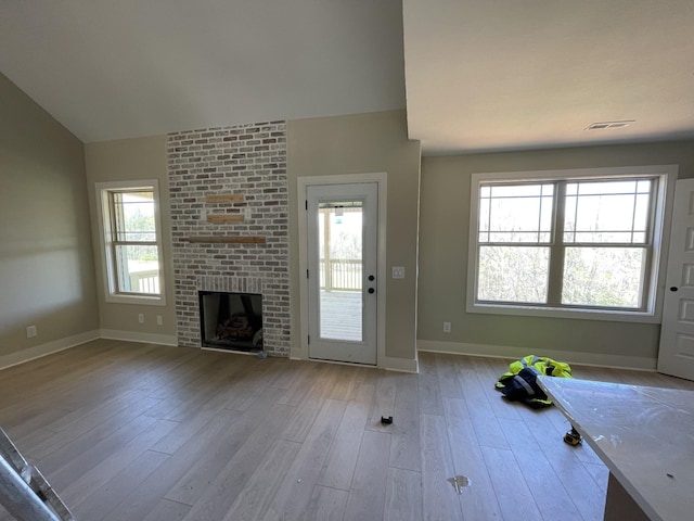 unfurnished living room with visible vents, baseboards, a brick fireplace, wood finished floors, and lofted ceiling