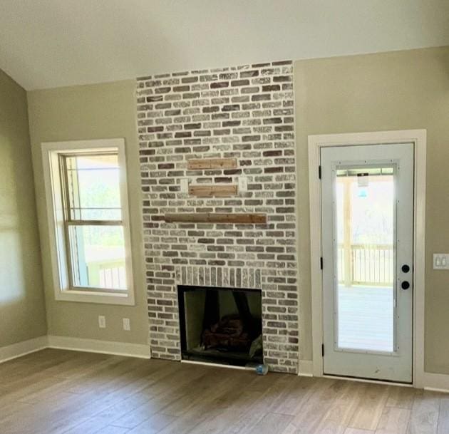 unfurnished living room with a brick fireplace, wood finished floors, and baseboards