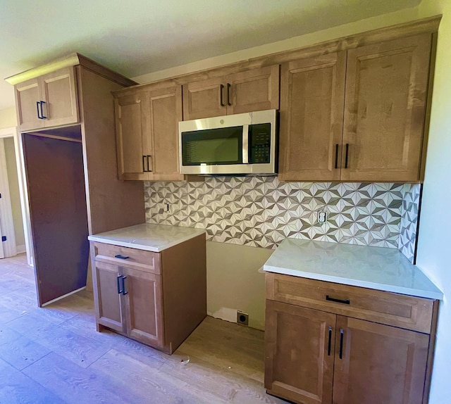kitchen with light wood-style flooring, stainless steel microwave, and backsplash
