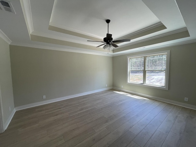 spare room with visible vents, baseboards, a ceiling fan, a tray ceiling, and wood finished floors