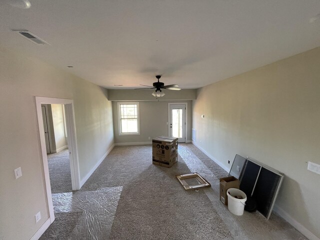 unfurnished living room featuring carpet, visible vents, baseboards, and a ceiling fan