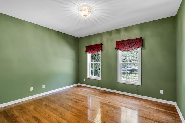 empty room featuring wood-type flooring and an inviting chandelier