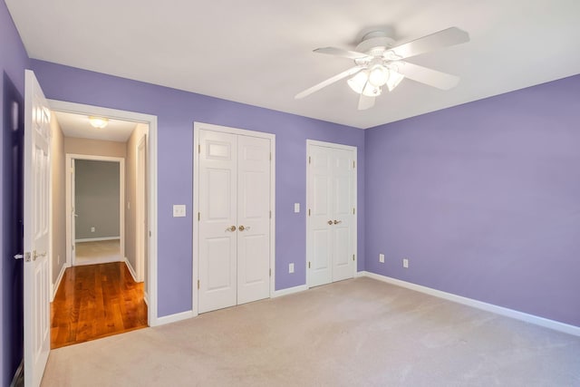 unfurnished bedroom with ceiling fan, two closets, and light colored carpet