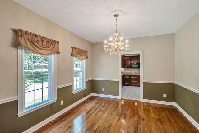 unfurnished dining area featuring an inviting chandelier and light hardwood / wood-style floors