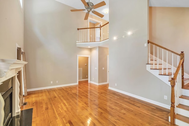 unfurnished living room with light wood-type flooring, ceiling fan, and a towering ceiling