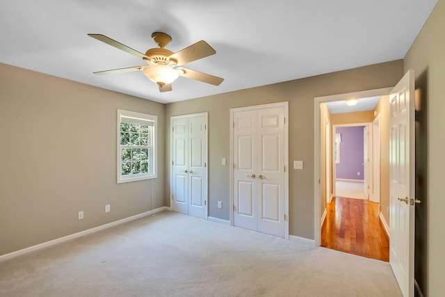 unfurnished bedroom with ceiling fan, light colored carpet, and two closets