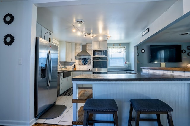 kitchen featuring appliances with stainless steel finishes, wall chimney range hood, decorative backsplash, kitchen peninsula, and a breakfast bar area