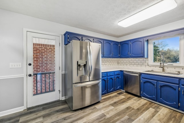 kitchen featuring appliances with stainless steel finishes, backsplash, blue cabinets, light hardwood / wood-style flooring, and sink