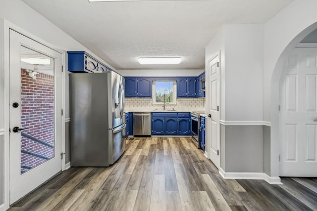 kitchen featuring stainless steel appliances, dark hardwood / wood-style floors, backsplash, blue cabinets, and sink