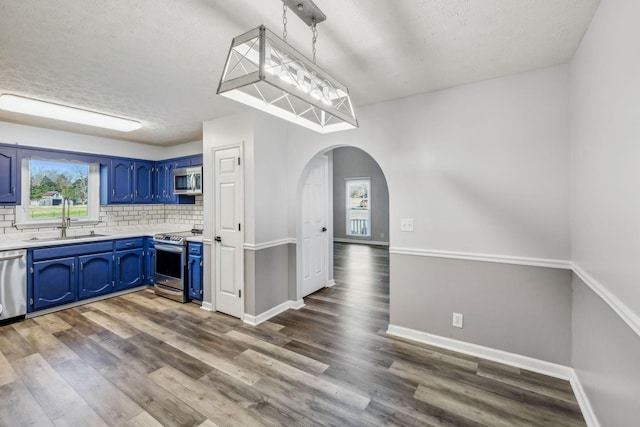 kitchen featuring appliances with stainless steel finishes, blue cabinetry, tasteful backsplash, hanging light fixtures, and sink