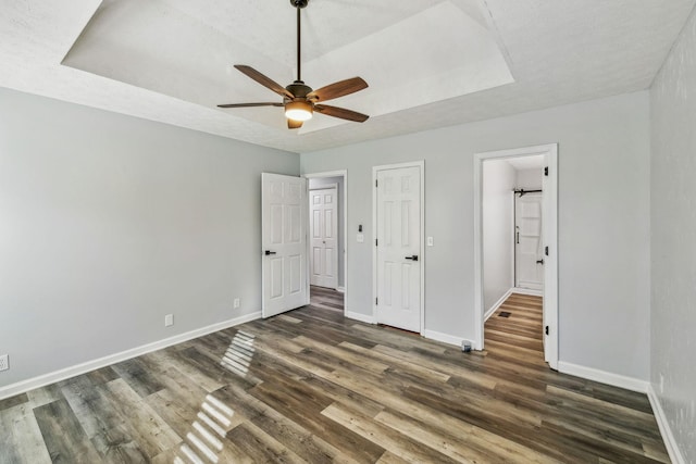 unfurnished bedroom with ceiling fan, dark hardwood / wood-style flooring, a textured ceiling, and a raised ceiling