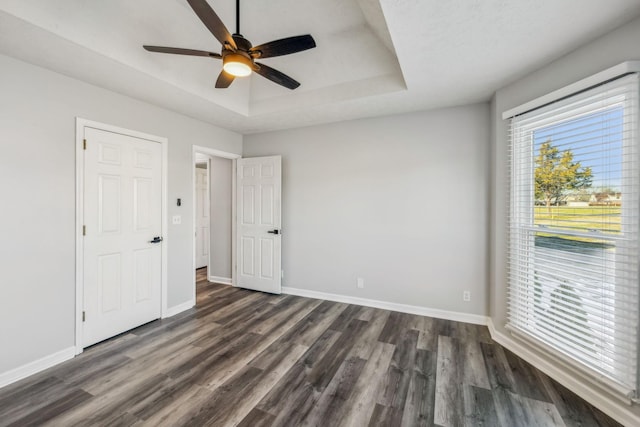 unfurnished bedroom with a raised ceiling, ceiling fan, and dark wood-type flooring