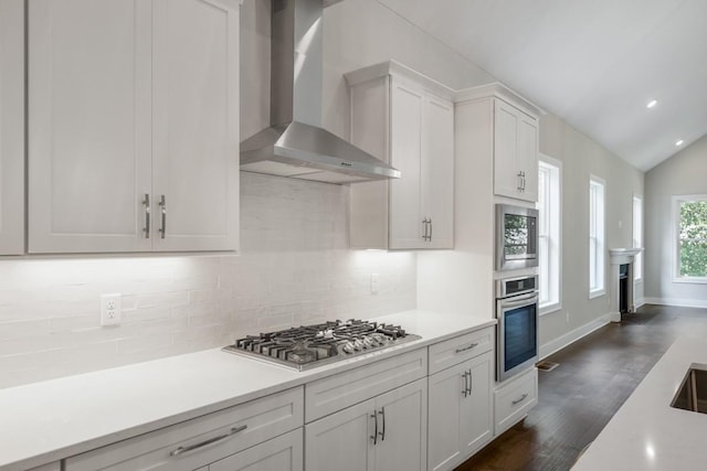 kitchen featuring dark wood-type flooring, white cabinetry, wall chimney range hood, stainless steel appliances, and vaulted ceiling