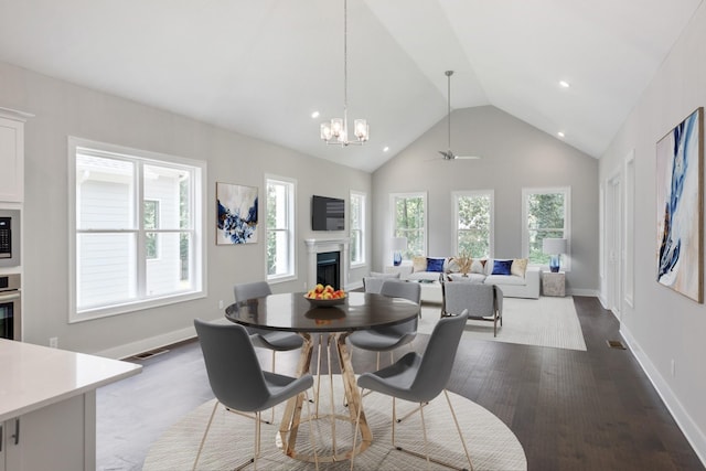 dining space with ceiling fan with notable chandelier, a wealth of natural light, wood-type flooring, and high vaulted ceiling