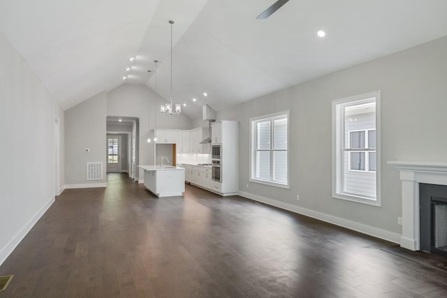 unfurnished living room featuring ceiling fan with notable chandelier, sink, high vaulted ceiling, and dark wood-type flooring