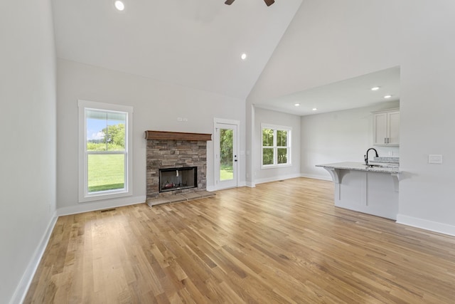 unfurnished living room with ceiling fan, a fireplace, sink, light hardwood / wood-style flooring, and high vaulted ceiling