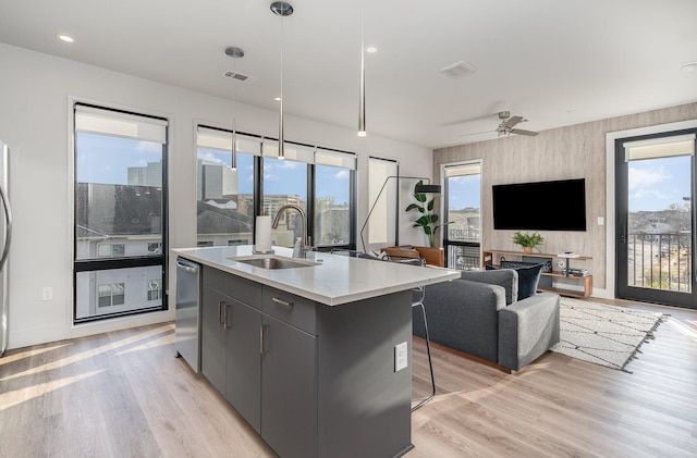 kitchen with sink, dishwasher, a kitchen island with sink, hanging light fixtures, and light wood-type flooring