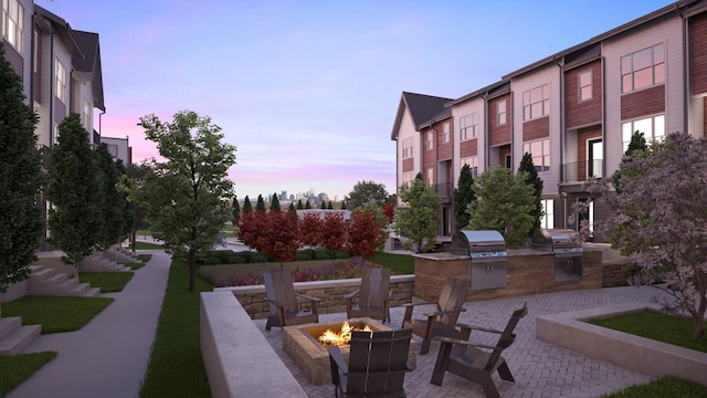 patio terrace at dusk featuring exterior kitchen, a grill, and a fire pit