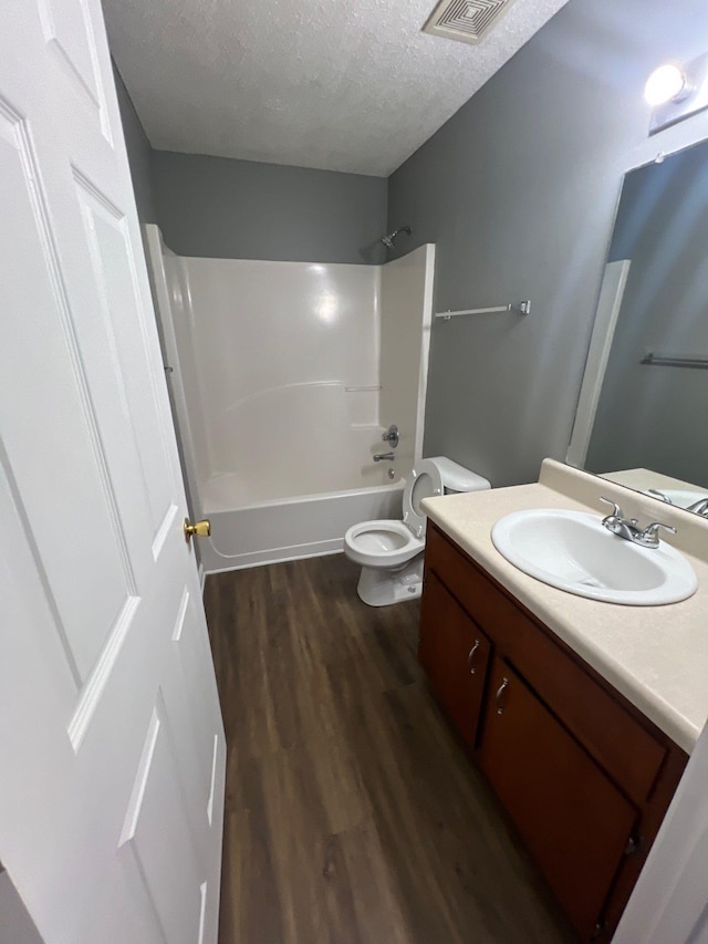 full bathroom with toilet, vanity, hardwood / wood-style floors, a textured ceiling, and bathing tub / shower combination