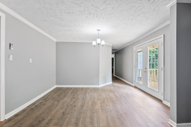 empty room featuring hardwood / wood-style flooring, ornamental molding, french doors, a textured ceiling, and a chandelier