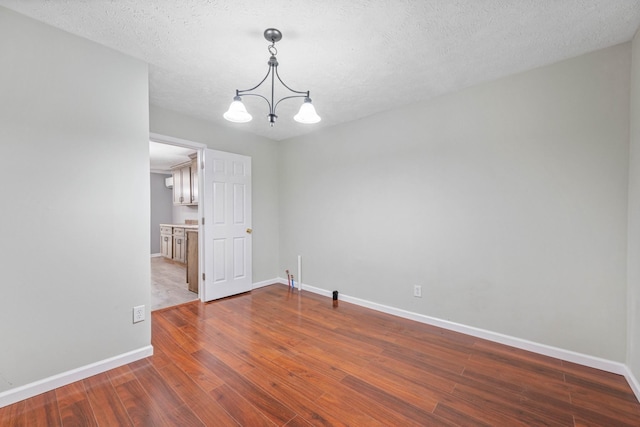 empty room with a textured ceiling, dark wood-type flooring, and an inviting chandelier