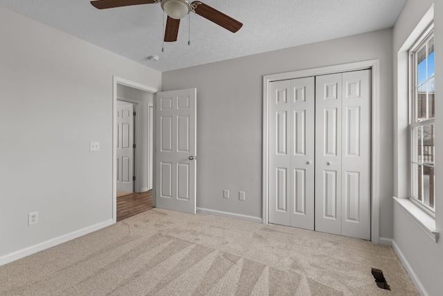 unfurnished bedroom with ceiling fan, light colored carpet, a closet, and a textured ceiling