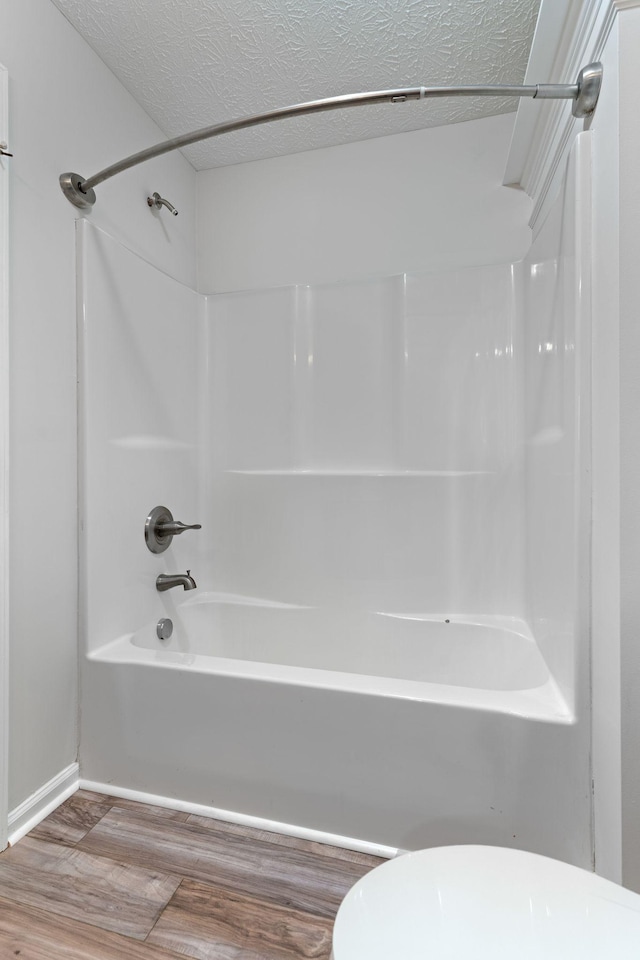 bathroom with wood-type flooring, toilet, bathing tub / shower combination, and a textured ceiling