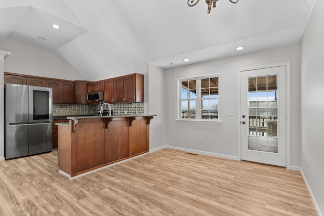 kitchen featuring vaulted ceiling, appliances with stainless steel finishes, tasteful backsplash, a kitchen bar, and kitchen peninsula