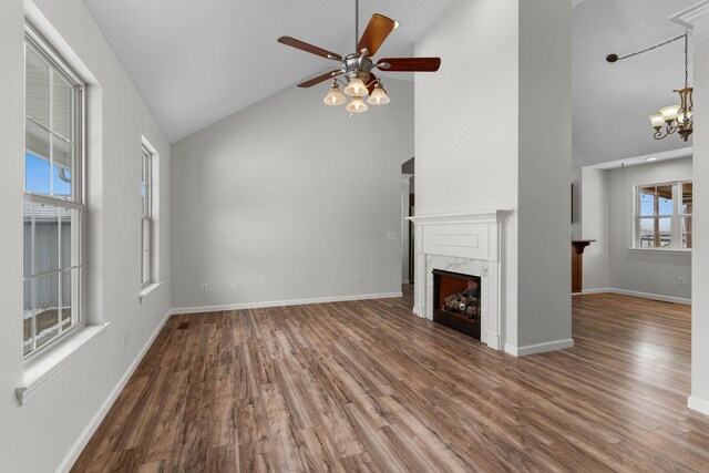 unfurnished living room featuring a premium fireplace, ceiling fan with notable chandelier, hardwood / wood-style floors, and high vaulted ceiling