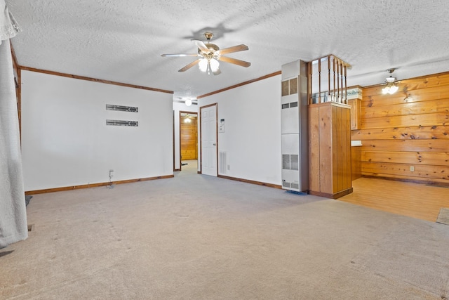 carpeted spare room featuring ceiling fan, ornamental molding, wooden walls, and a textured ceiling