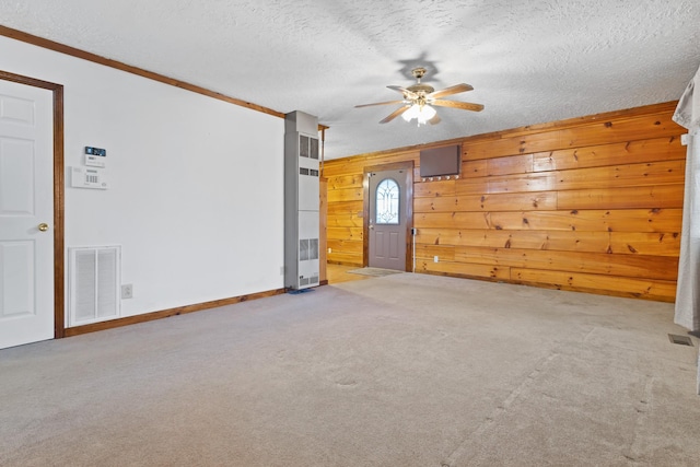 unfurnished room featuring wood walls, carpet flooring, ceiling fan, crown molding, and a textured ceiling