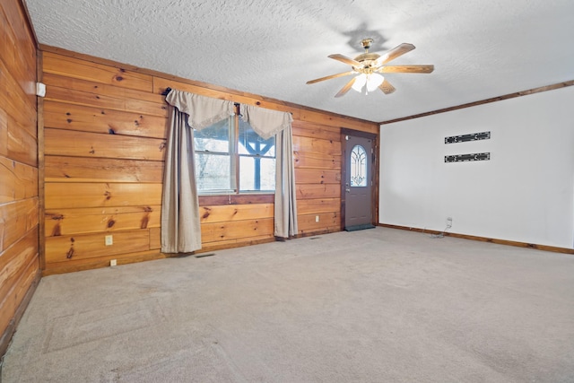 unfurnished room featuring light carpet, ornamental molding, a textured ceiling, and wood walls