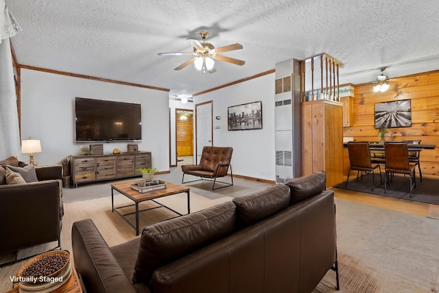 living room featuring crown molding, a textured ceiling, ceiling fan, and wood walls