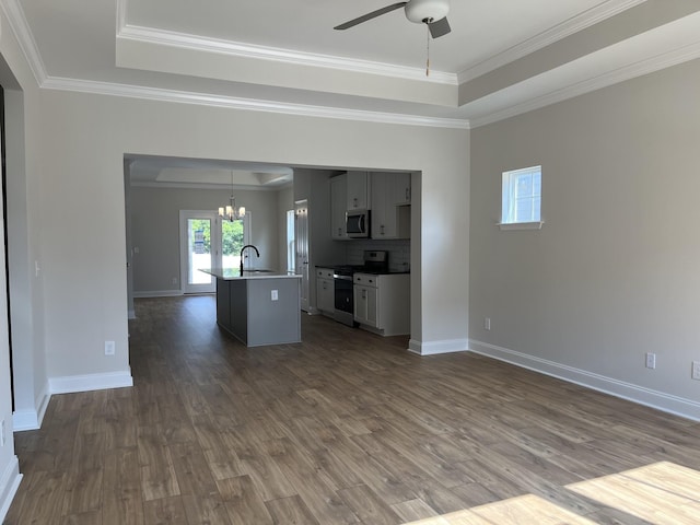 unfurnished living room with ceiling fan with notable chandelier, sink, a tray ceiling, and dark wood-type flooring