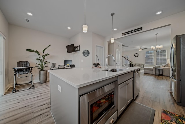 kitchen with decorative light fixtures, sink, light hardwood / wood-style floors, stainless steel appliances, and a center island with sink