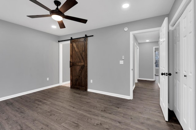 unfurnished bedroom featuring ceiling fan, a closet, dark hardwood / wood-style flooring, and a barn door