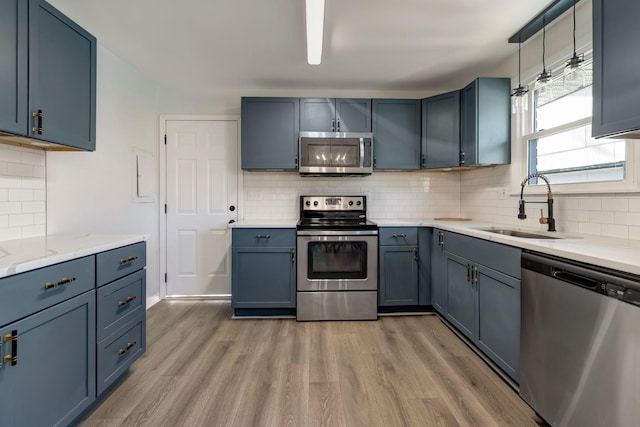 kitchen with stainless steel appliances, tasteful backsplash, sink, blue cabinetry, and hardwood / wood-style flooring