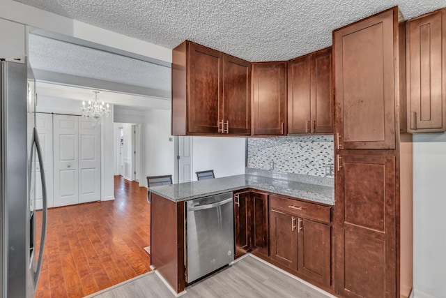 kitchen with decorative light fixtures, light wood-type flooring, light stone countertops, and stainless steel appliances